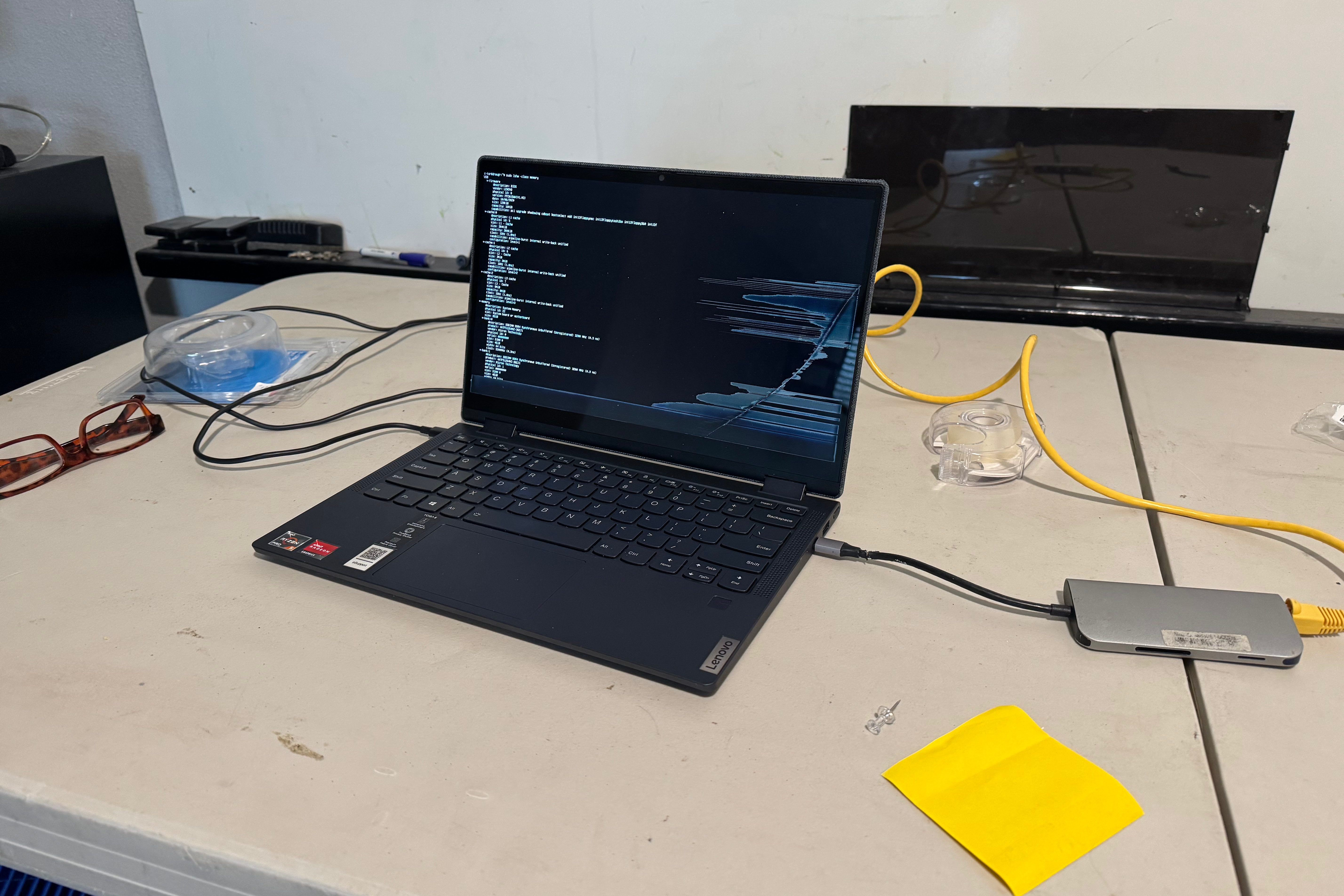 A laptop with a broken screen with a power and ethernet cable running to it, displaying an ubuntu command line